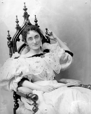 Clara Lowenberg Moses in gown, seated in a carved wooden chair.