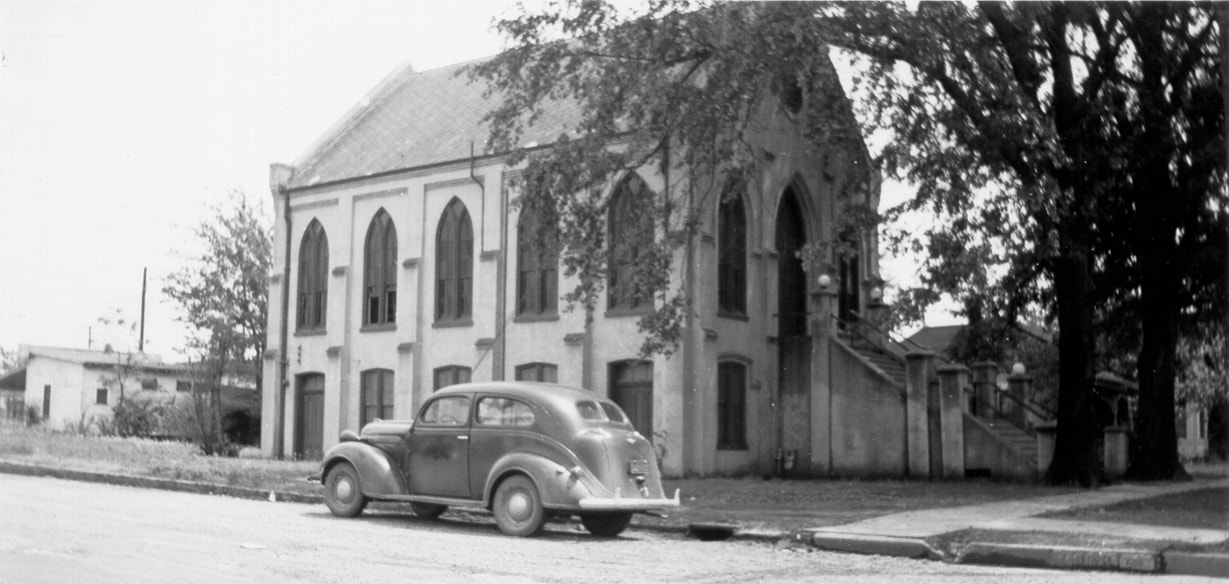 Three quarter view of the gothic-style, two-story synagogue, with an automobile parked on the street.