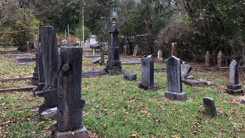 Three rows of headstones in various states of disrepair. The closest headstone resembles a cut tree trunk.