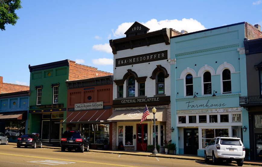 A row of storefronts in Canton, Mississippi. Second from the right is the a three story building, white with brown trim. Signs read 
