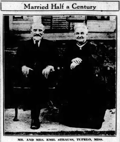 An older man and woman, seated in dark, formal clothes. Text: 