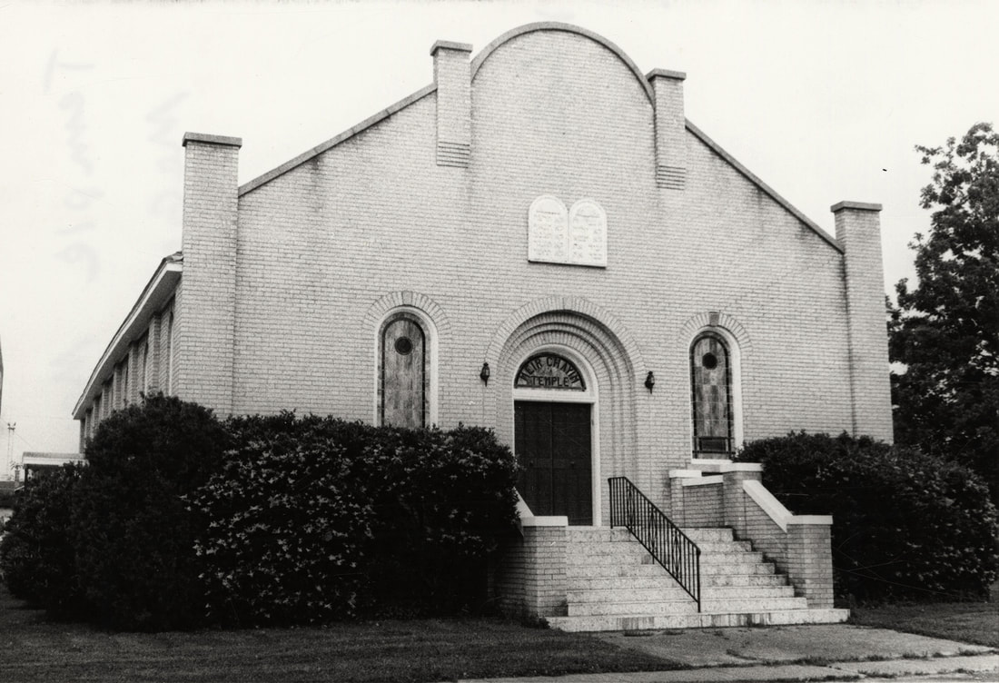 Black and white photograph of a modest, brick, gothic synagogue. 